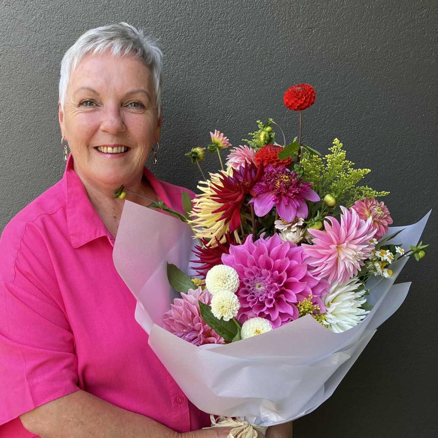 Woman in a pink shirt holding a bouquet of flowers against a dark background